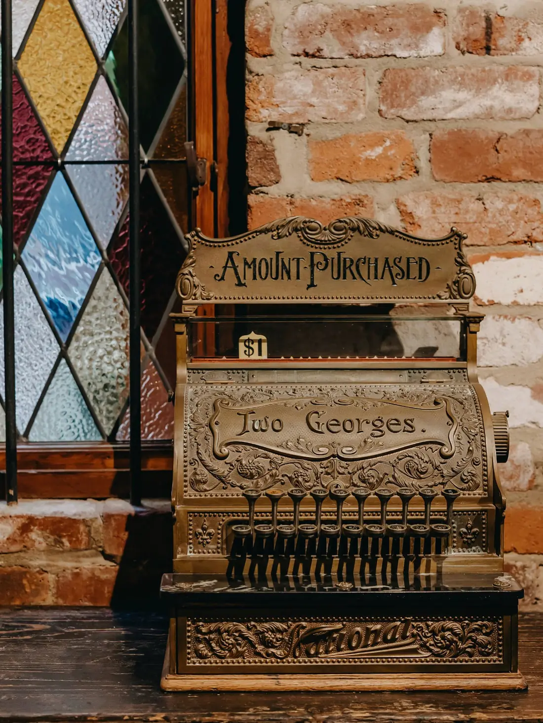 The antique brass Two Georges cash register beside the leadlight window, Fremantle